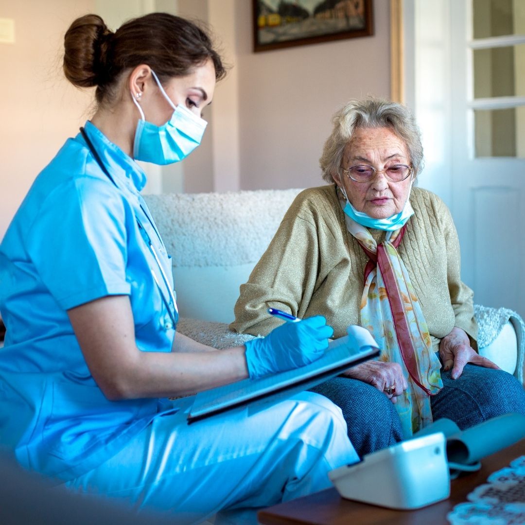 Enfermeira realiza atendimento domiciliar com idosa, anotando informações de saúde durante acompanhamento no home care, voltado à prevenção de doenças cardiovasculares em idosos.