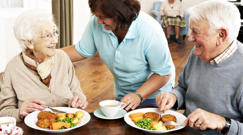 Idosos recebem refeição balanceada com acompanhamento de cuidadora, representando a importância da nutrição no controle de colesterol no home care.