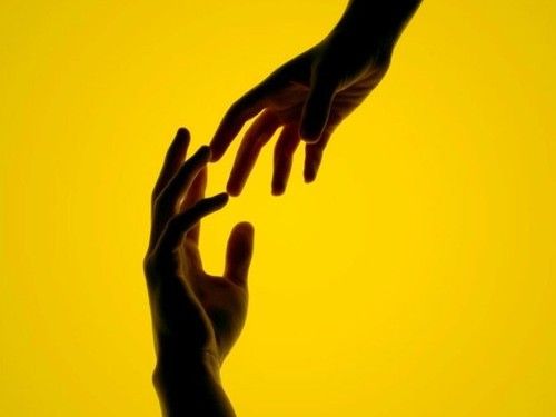 Duas mãos se estendendo em direção uma à outra sobre fundo amarelo, simbolizando apoio, esperança e valorização da vida.